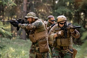 Group of attentive armed soldiers in camouflage outfits moving with rifles in forest while working at clean-up operation