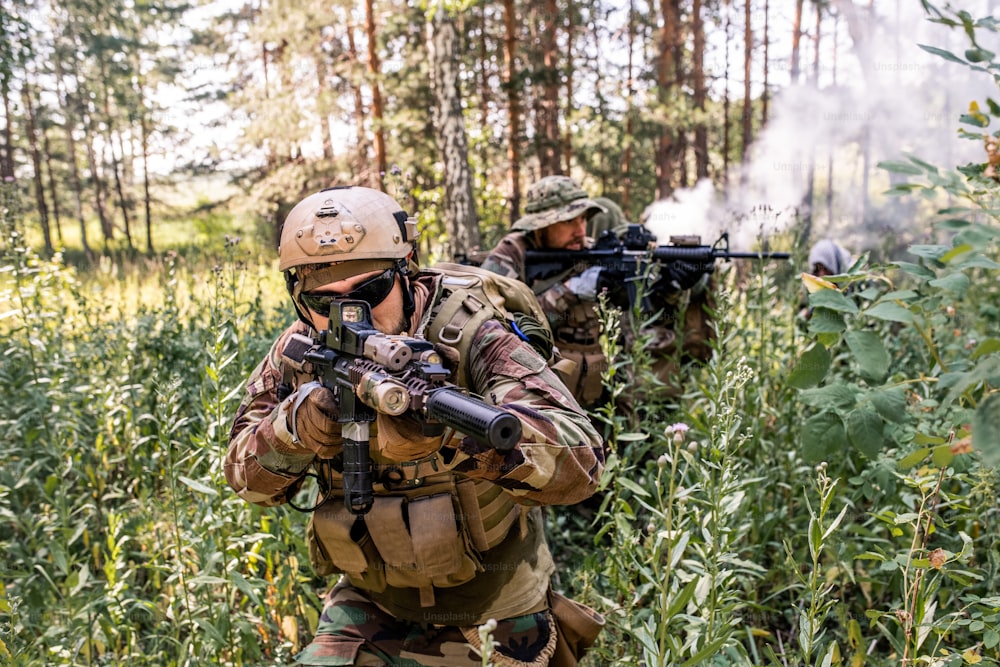 Grupo de soldados uniformados moviéndose a través de arbustos forestales mientras realizan una operación de reconocimiento militar