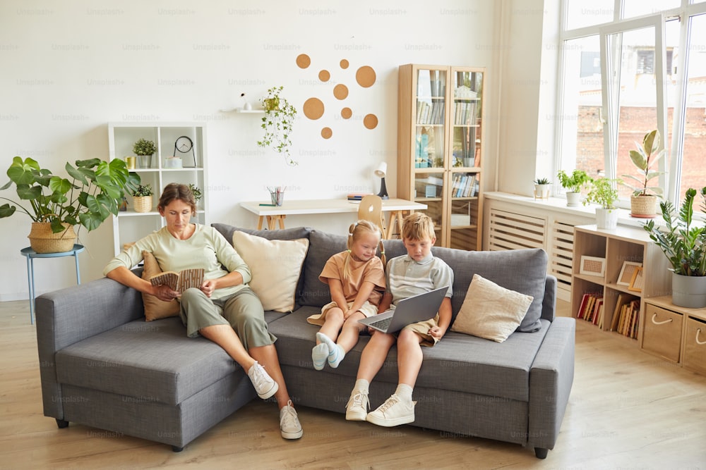 Full length portrait of modern family with special needs child sitting together on sofa in home interior, copy space