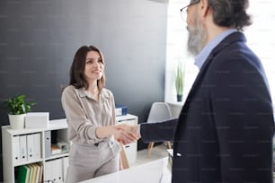 Confident young woman greeting mature HR manager with handshake before starting job interview