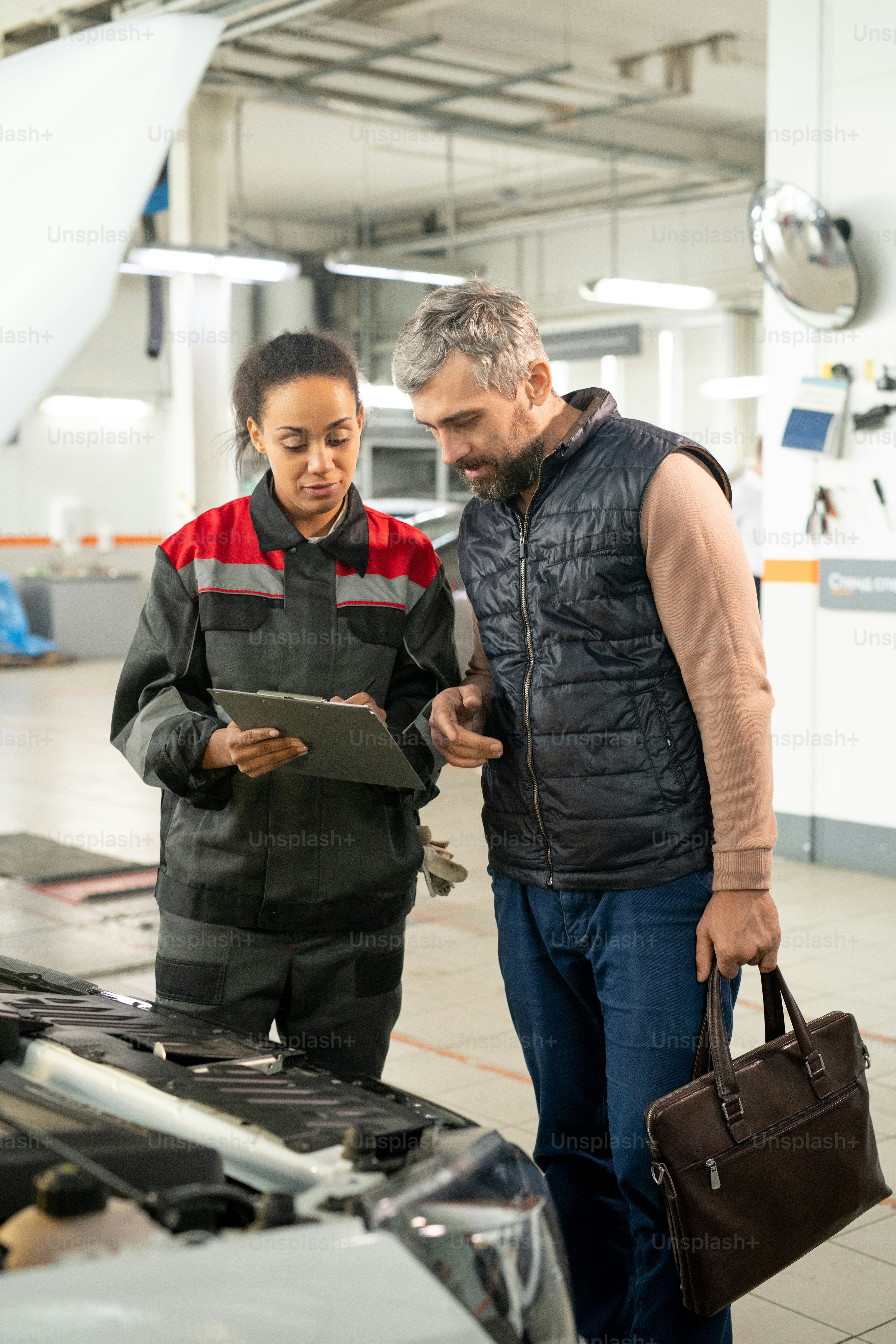 Young female technician of car repair service pointing at document ...