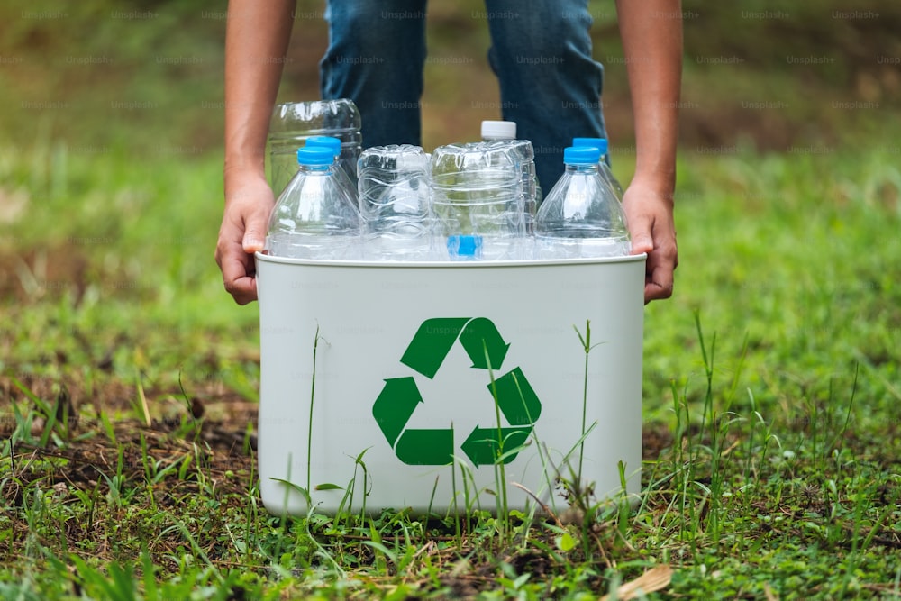 Una mujer sosteniendo una papelera de reciclaje con botellas de plástico al aire libre