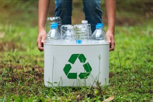 Une femme tenant un bac de recyclage avec des bouteilles en plastique à l’extérieur