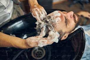 Foto recortada de un cliente con champú y lavado en una barbería bien equipada