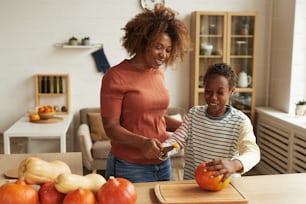 Modern young mother and her child standing together at table starting carving pumpkins for Halloween