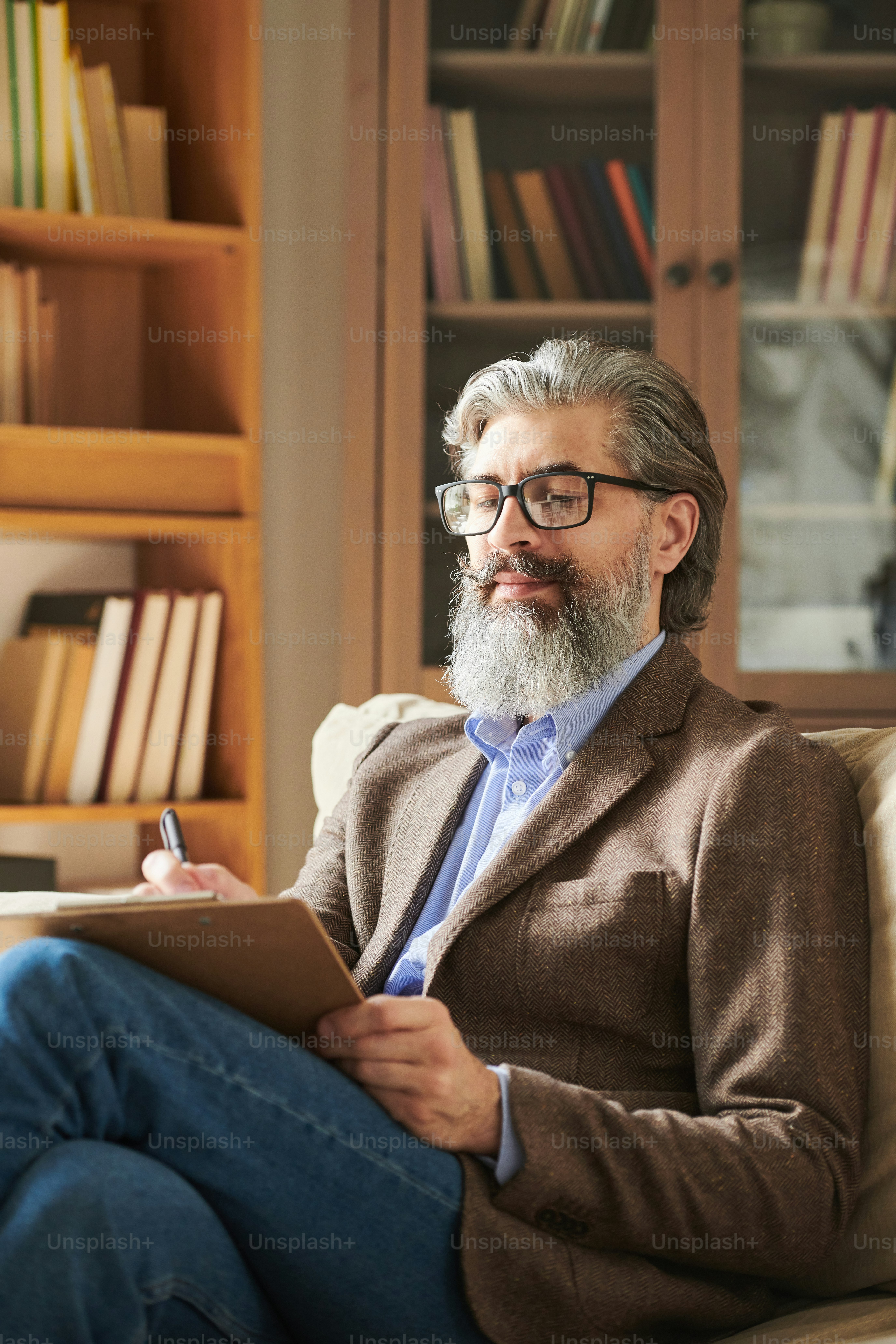 Foto média vertical de homem barbudo bonito vestindo roupa elegante sentado no sofá na sala de escritório moderna fazendo anotações