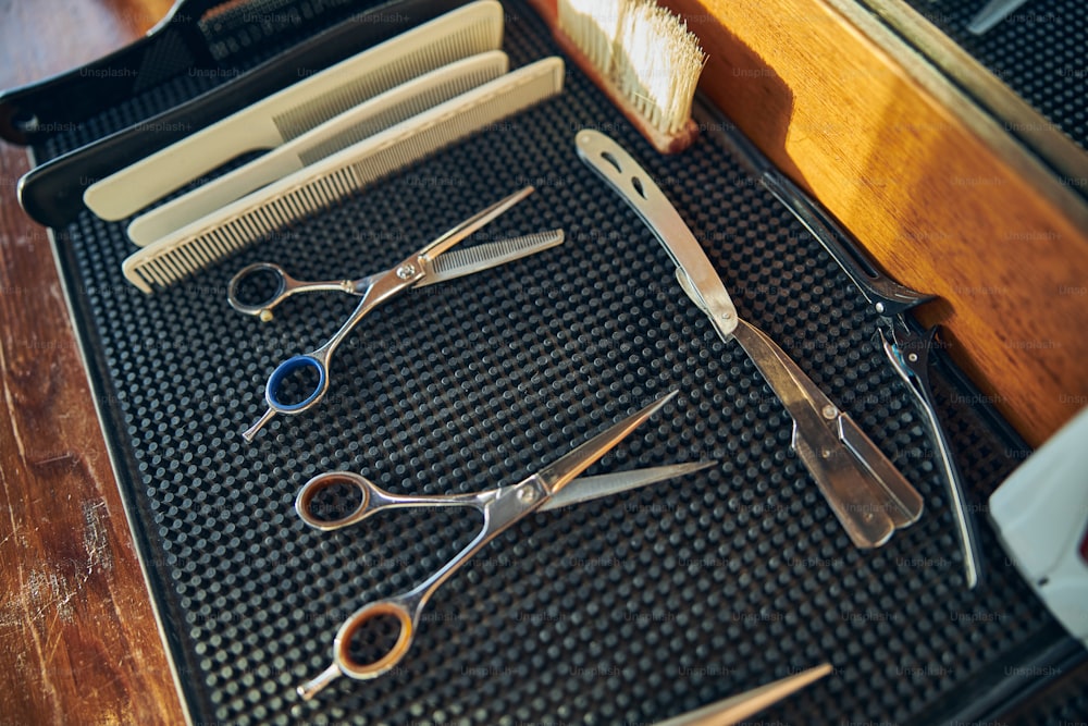 No people photo of a neat setup of barbering scissors, hair combs and clippers on a black rubber sheet