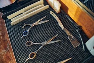 No people photo of a neat setup of barbering scissors, hair combs and clippers on a black rubber sheet