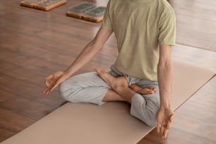 Jeune homme en tenue de sport en équilibre assis sur le tapis dans la pose du lotus et en pratiquant des exercices de méditation à la maison