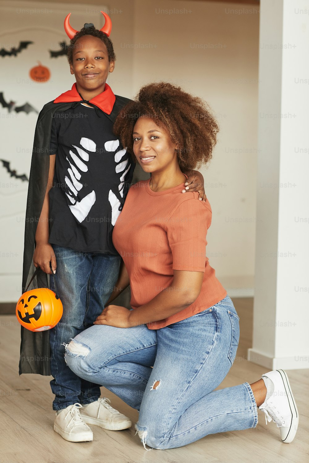 Vertical full shot of beautiful woman and her preteen son wearing little devil costume for Halloween looking at camera