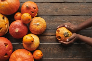 Directamente desde arriba, la vista plana yacía una foto de calabazas y mandarinas talladas con caras de linterna de jack o' y manos de mujer sosteniendo una calabaza para Halloween sobre un fondo de mesa de madera oscura ...