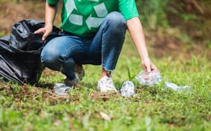 リサイクルのコンセプトのために公園でゴミのペットボトルをビニール袋に入れる女性活動家の接写画像