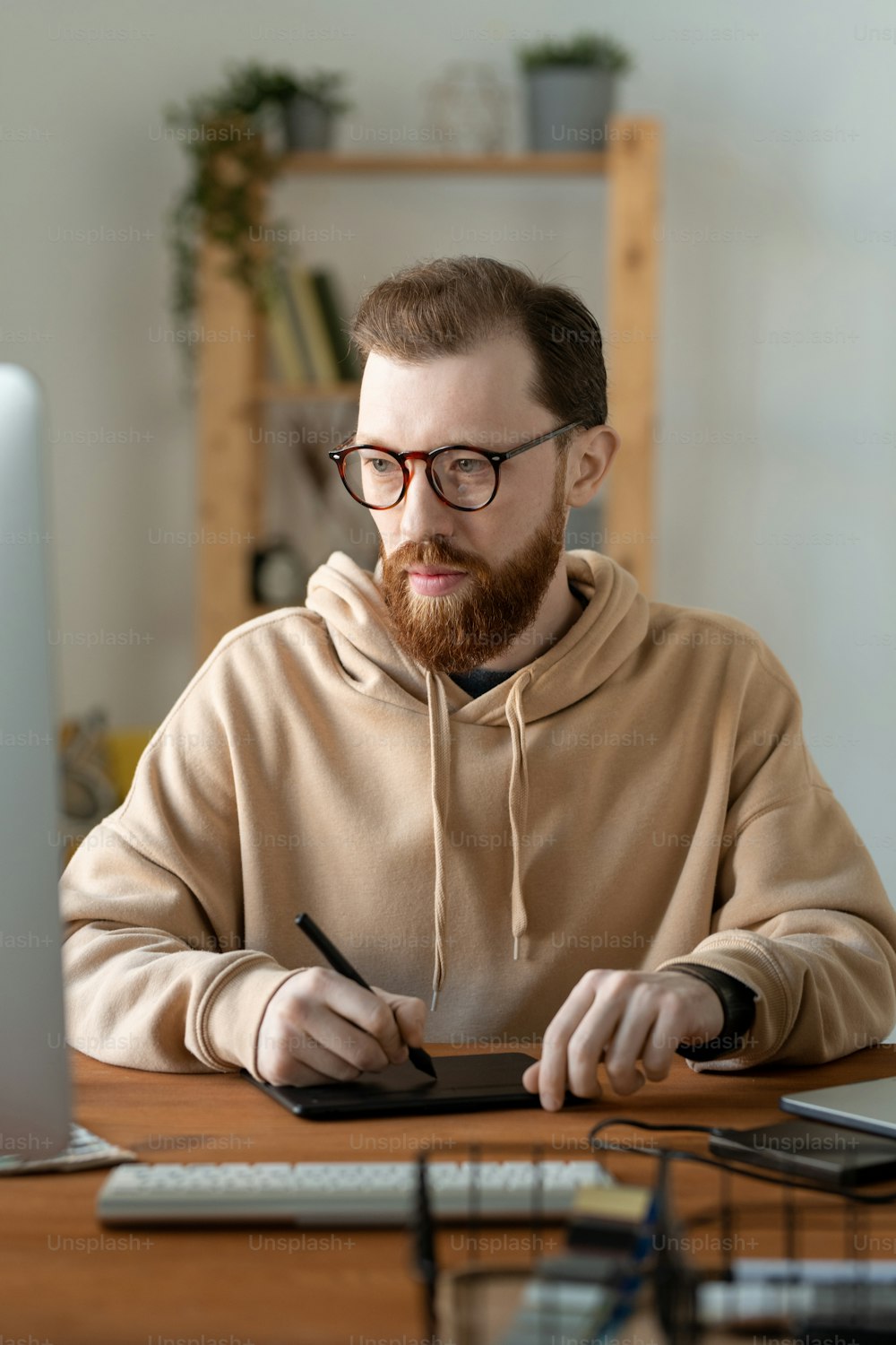 Young contemporary serious freelancer in eyeglasses and casualwear using touchpad and stylus while retouching images on computer screen