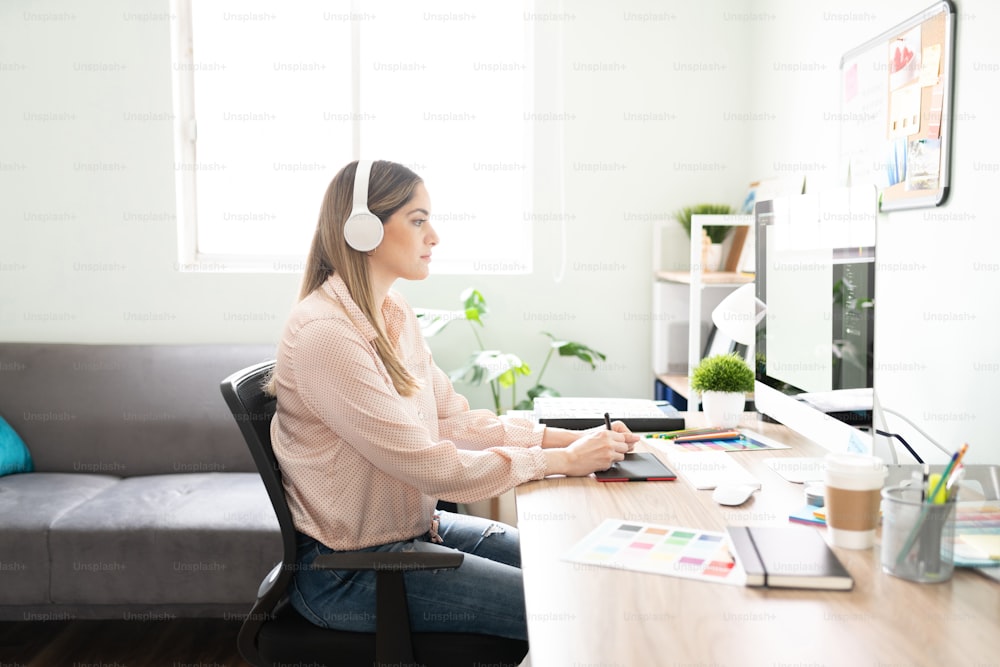 Profile view of a female graphic designer and illustrator looking really focused while drawing and listening to music in her office