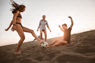 夏休みに素晴らしい家族の時間を過ごすビーチでサッカーをする幸せな家族。