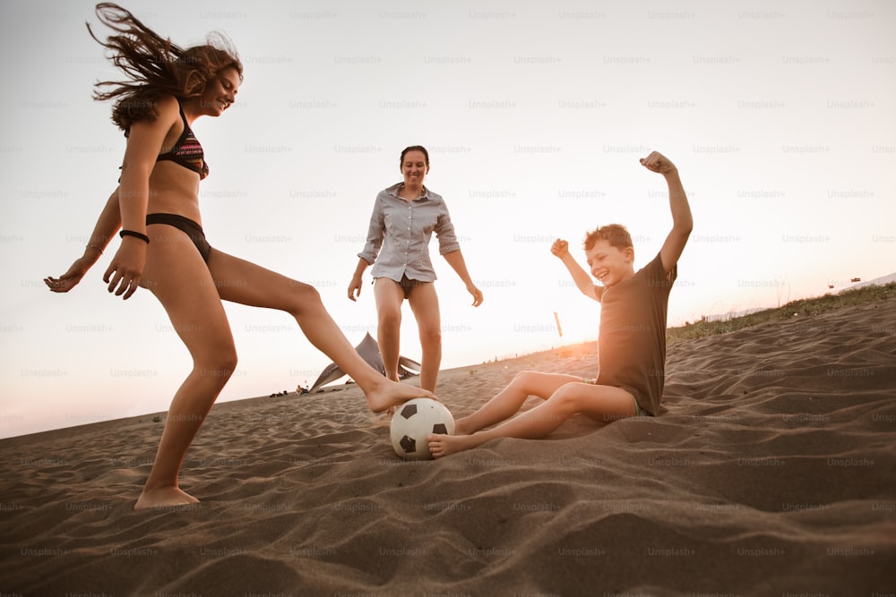 Familia feliz jugando al fútbol en la playa teniendo un gran tiempo en familia en las vacaciones de verano.