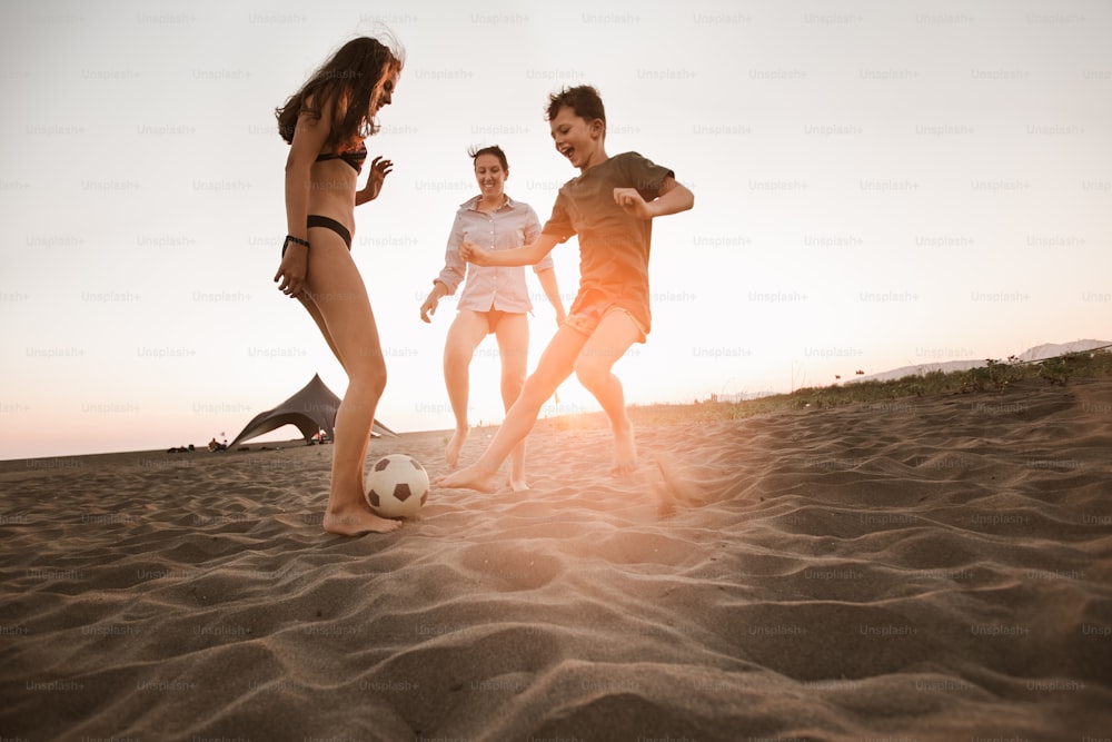 Glückliche Familie, die Fußball am Strand spielt und in den Sommerferien eine tolle Zeit mit der Familie hat.
