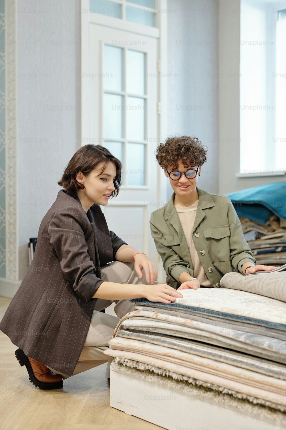 Junge elegante Verkäuferin, die Kunden bei der Auswahl eines Musters neuer Teppiche oder Bodenbeläge in einem zeitgenössischen Studio für Innenarchitektur berät