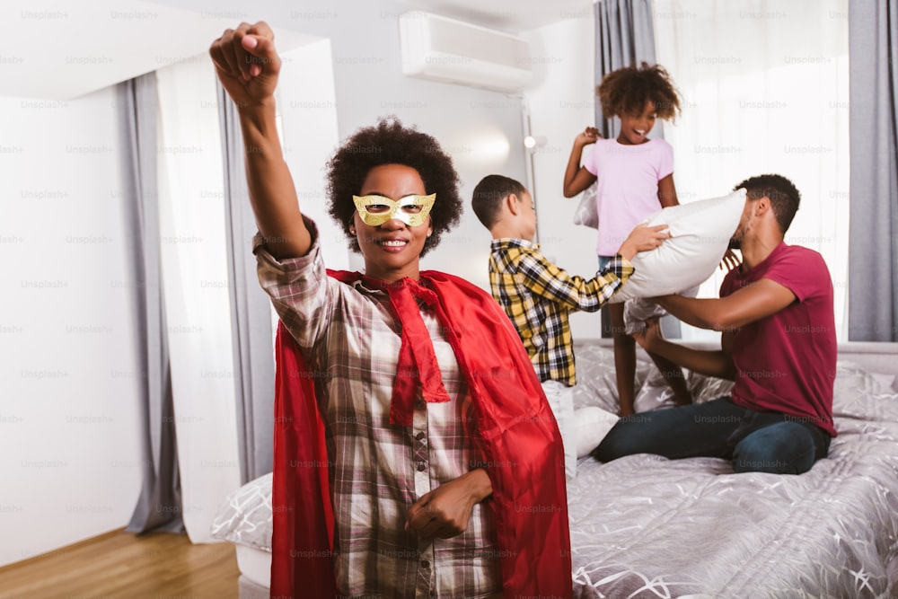 Playful mother in superhero costume playing at home with family
