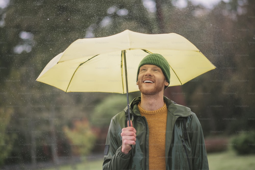 Under umbrella. Young bearded man standing with yellow umbrella in hand