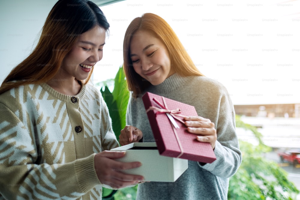 Mulheres asiáticas jovens felizes abrindo uma caixa de presente juntos