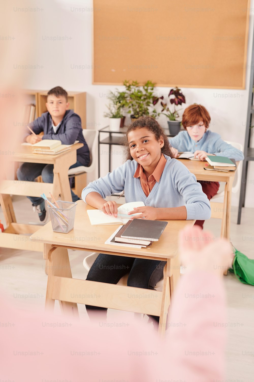 Des élèves interculturels heureux du secondaire en tenue décontractée regardant l’enseignante et l’écoutant assise près des bureaux dans une grande salle de classe