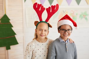 Retrato de niño y niña con sombreros de Santa Claus y mirando a la cámara mientras disfruta de la clase en Navidad, copie el espacio