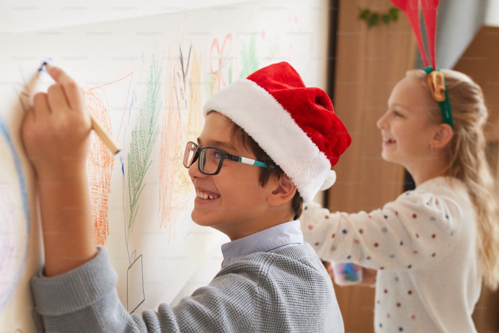 Side view portrait of boy and girl drawing on walls while wearing Santa hats for Christmas, copy space
