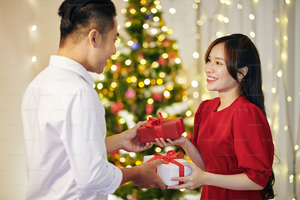 Beautiful smiling young Vietnamese couple exchanging Christmas presents at home