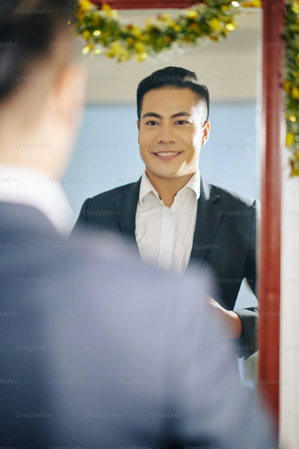 Feliz y elegante joven vietnamita parado frente al espejo cuando se pone un traje elegante