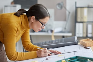 Side view portrait of female architect drawing blueprints while working at desk in office, copy space