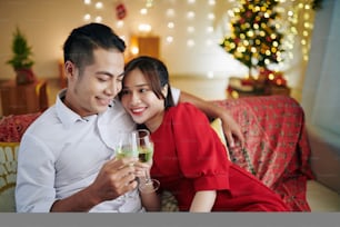 Beautiful young Asian couple in love spending Christmas night at home and drinking champagne