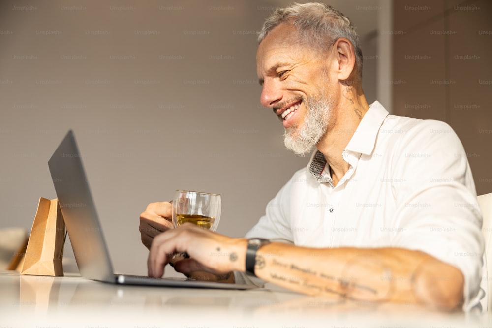 Empreendedor pressionando as teclas em um teclado de laptop e tomando um chá em uma sala iluminada pelo sol