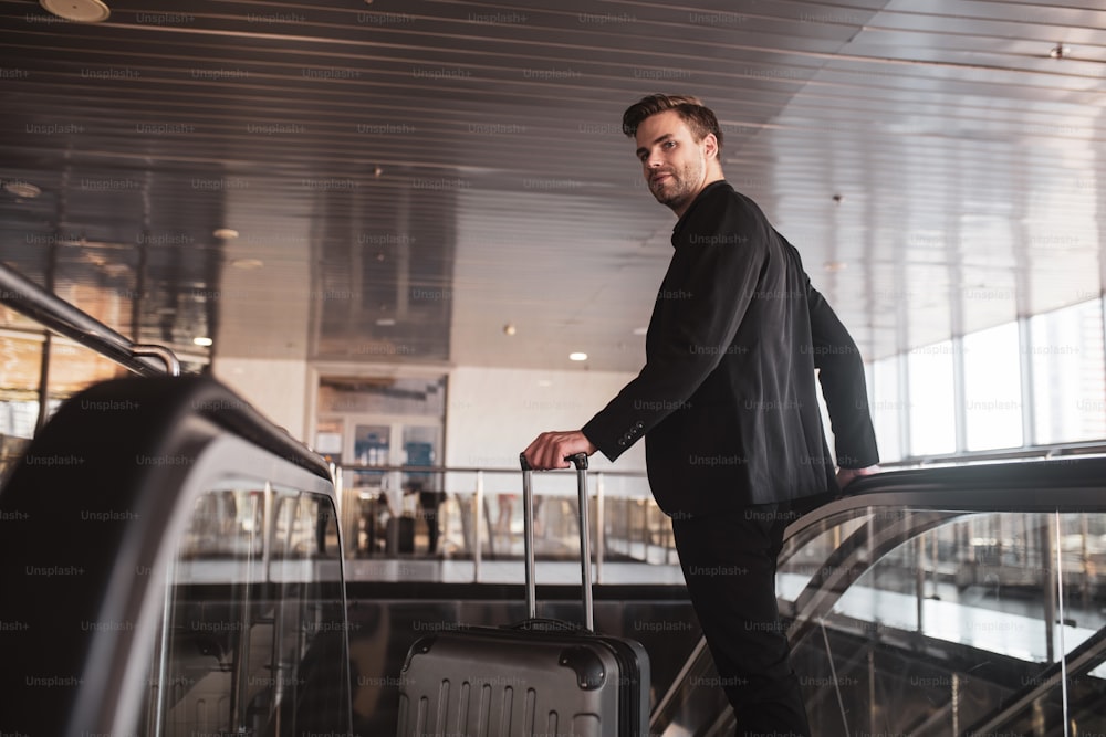 Convenient airport. A man holding the suitcase and using the escalator