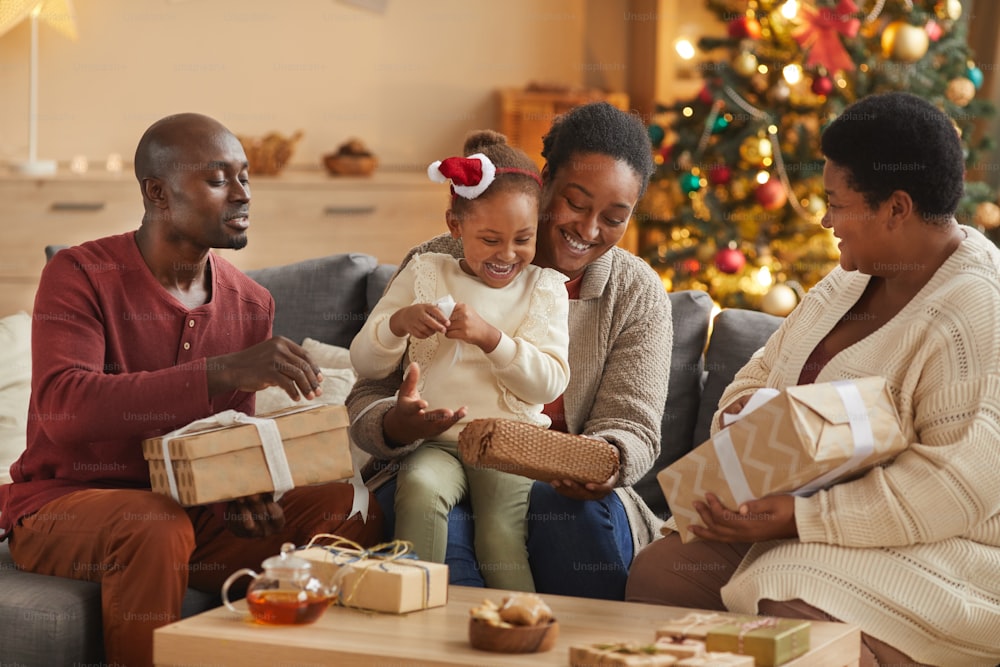 Warmes Porträt einer glücklichen afroamerikanischen Familie, die Weihnachtsgeschenke öffnet, während sie die Weihnachtszeit zu Hause genießt