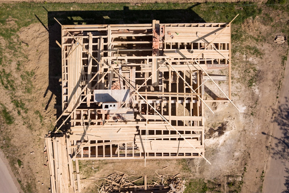 Aerial view of unfinished brick house with wooden roof frame structure under construction.