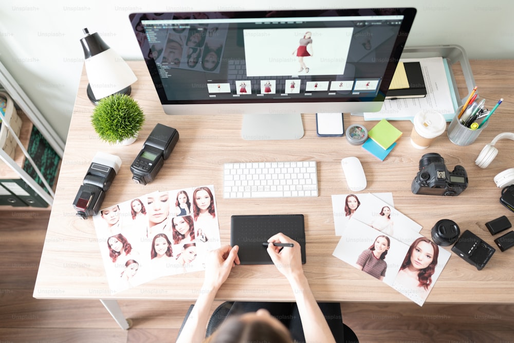 Top view of the workspace of a photographer with a camera, equipment, computer, prints, a graphic tablet and more.