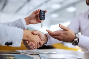 Closeup of car seller and buyer shaking hands. Car seller handing a car keys to a buyer. Car salon interior.