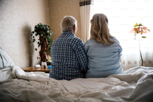 Elderly couple. Caucasian senior elder couple sitting on the bed and looking to the window. Retirement family lifestyle concept