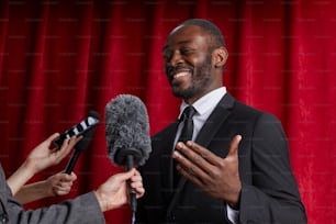 ジャーナリストにインタビューを行い、赤いカーテンに向かってマイクに話す笑顔のアフリカ系アメリカ人男性の腰のポートレート