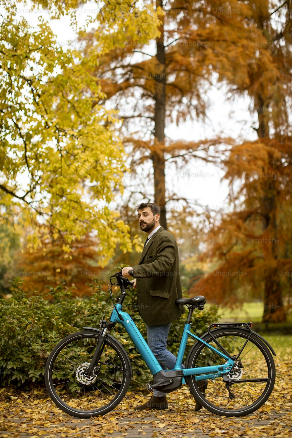 Apuesto joven con bicicleta eléctrica en el parque de otoño