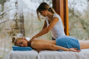 Beautiful young woman lying and having neck massage in spa salon during winter season