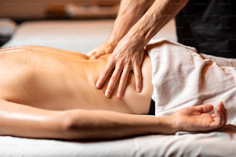 Homem recebendo uma massagem profunda nas costas de terapeuta profissional em salão de spa de luxo