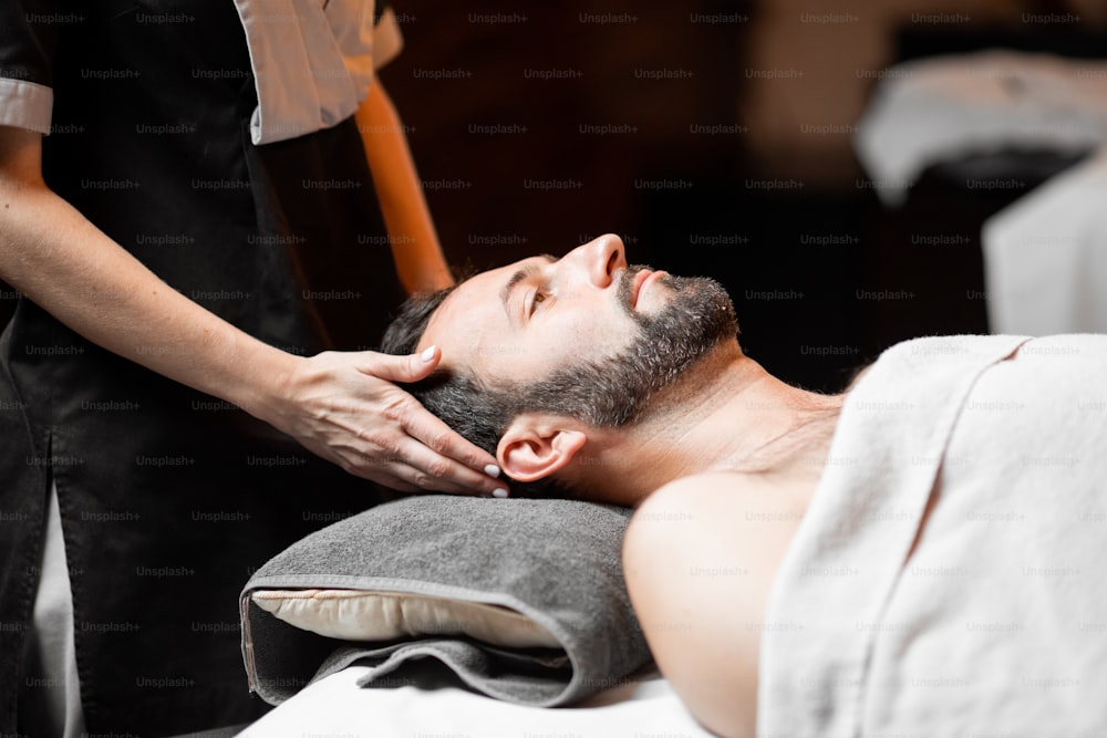 Hombre barbudo recibiendo un masaje facial, relajándose en el salón Spa, primer plano