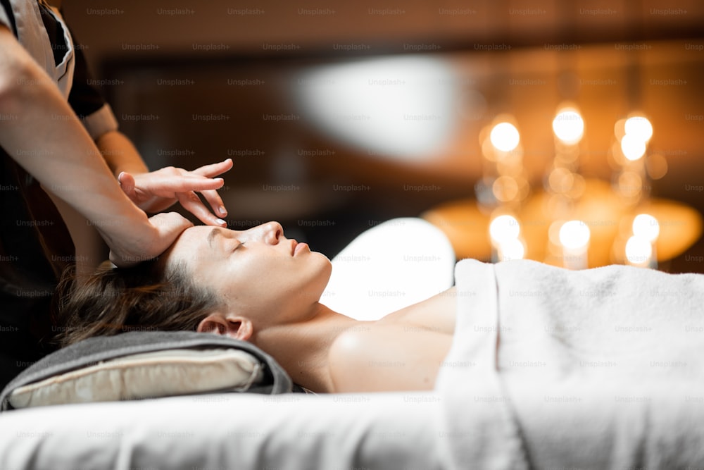 Mujer joven recibiendo un masaje facial, relajándose en el salón de spa