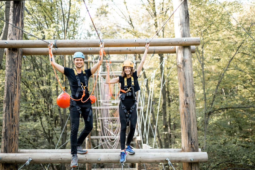 Well-equipped man and woman having an active recreation, climbing ropes in the park with obstacles outdoors