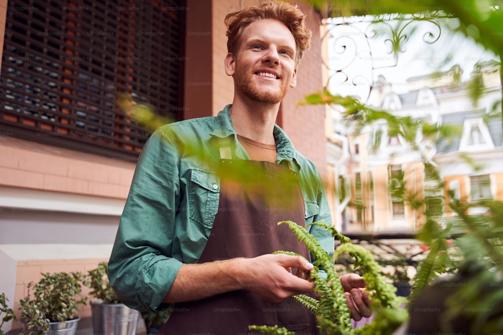 Portrait of handsome red head barista taking care about plants in cafe yard