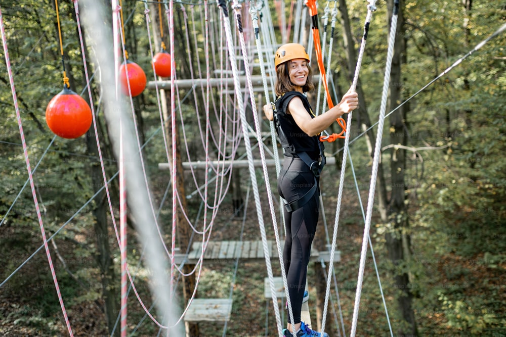 Young well-equipped woman having an active recreation, climbing ropes in the park with obstacles outdoors