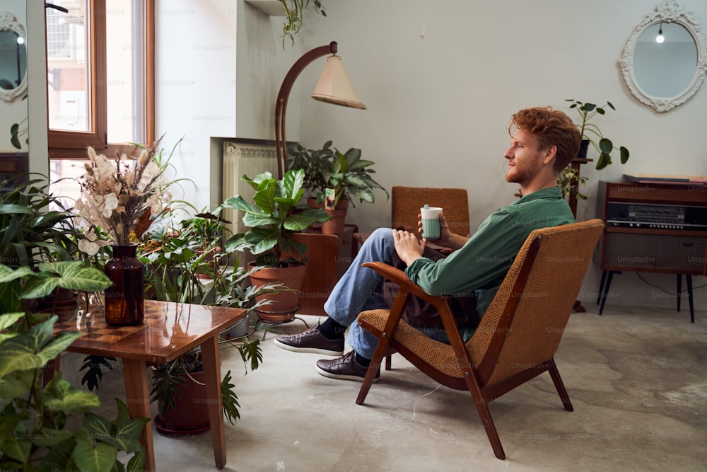 Handsome red head florist sitting on chair drinking coffee in flower shop