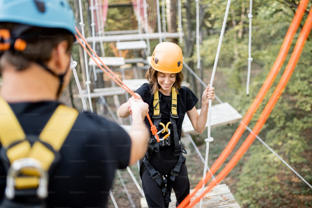 Well-equipped man and woman having an active recreation, climbing ropes in the park with obstacles outdoors